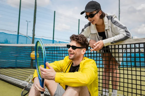 happy man and woman in active wear resting near tennis net on court, sportswear fashion, sport
