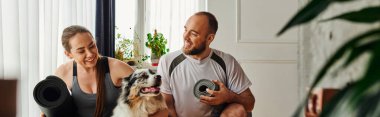Spor kıyafetleri içinde gülümseyen bir kadın spor kıyafetleri içinde spor minderi tutuyor ve evdeki adamın yanında Sınır Çobanı 'na sarılıyor.