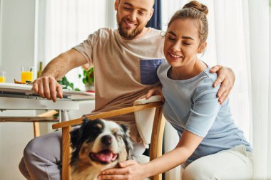 Gülümseyen bir çift sabahları evde kahvaltı yaparken çoban köpeğini okşuyor.