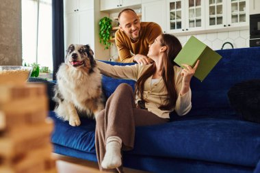 Gülümseyen çift oturma odasındaki patlamış mısırın yanındaki kanepede kitap ve sınır köpeğiyle vakit geçiriyor.