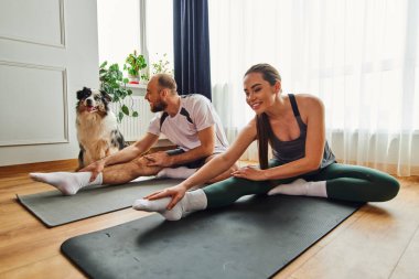 Spor giyim antrenmanında gülümseyen bir kadın. Erkek arkadaşıyla birlikte. Evde, border collie 'nin yanında spor minderleri üzerinde.