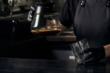 Siyah eldivenli barista elinde bardak ve kahve demliği taze demlenmiş espresso.