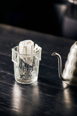 Dökümlü demleme metodu, kağıt filtre torbalı cam ve siyah masa üstünde metalik su ısıtıcısı