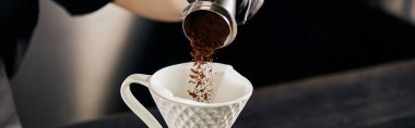 Kahveci jigger 'dan seramik damlatıcıya, V-60 tarzı espresso damlasına, pankarta ince öğütülmüş kahve ekliyor.