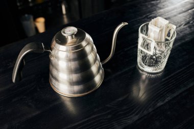 Metalik su ısıtıcısı, öğütülmüş kahve kaplı kristal bardak siyah masa üzerinde filtre poşet, damlatma yöntemi