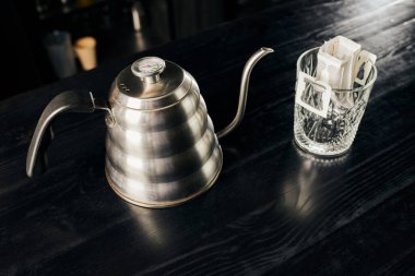 metallic drip kettle, crystal glass with ground coffee in filter bag on black table, drip method clipart