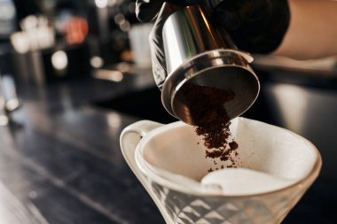 Barista V-60 tarzı espresso hazırlıyor, seramik damlatıcıya filtreli öğütülmüş kahve dolduruyor.