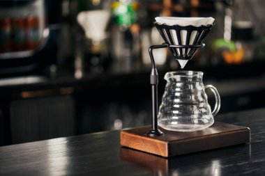 V-60 tarzı metot, damlalar siyah ahşap tezgahta cam kahve demliğinin üzerinde filtre torbasıyla duruyor.