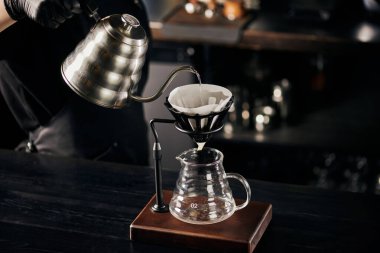 V-60 tarzı espresso birası, barista bardağa kaynar su döküyor damlatma tezgahının üzerine.