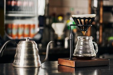 V-60 tarzı espresso birası, su damlası, kağıt filtresi olan damlatıcı tutacağı, siyah tezgahta kahve demliği.