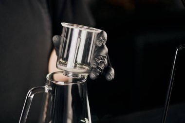 Kahve dükkanı, siyah lateks eldivenli barista kısmi görüntüsü cam demliğin üzerinde sifon kahve makinesi tutuyor.