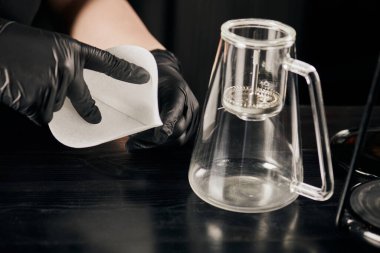Siyah lateks eldivenli kahve makinesinin yanında kağıt filtre tutan barista manzarası.