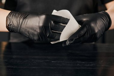 Siyah lateks eldivenli barista 'nın siyah masanın üzerinde kahve için kağıt filtre poşeti tutarken kısmi görüntüsü