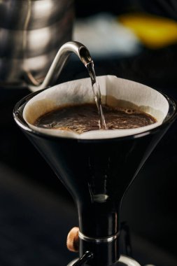 Kaynar su çaydanlıktan sifonlu kahve makinesine kağıt filtresi ve köpüklü kahve ile doluyor.