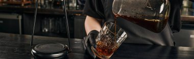 Kahve makinesinden kristal bardağa, pankarta taze demlenmiş espresso dökülen baristanın kısmi görüntüsü