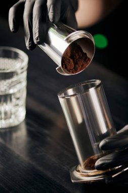 Siyah lateks eldivenli barista. Aero press 'e öğütülmüş kahve koyuyor. Alternatif demleme yöntemi.