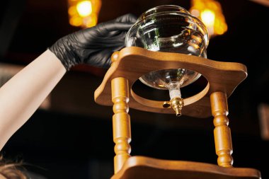 Siyah lateks eldivenli baristanın düşük açılı görüntüsü modern kahve dükkanındaki soğuk kahve makinesini ayarlıyor.