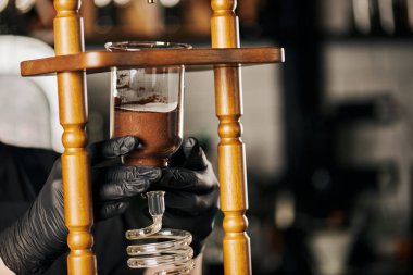 Siyah lateks eldivenli barista soğuk damlalı kahve makinesinin parçalarını birleştiriyor, alternatif kahve demliyor. 