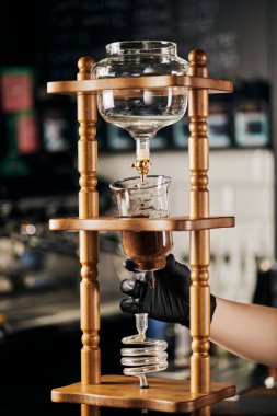 Siyah eldivenli barista soğuk kahve makinesini öğütülmüş kahveyle birleştiriyor. Alternatif espresso.