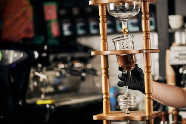 Alternatif espresso demleme yöntemi, siyah eldivenli barista kafedeki soğuk damlalı kahve makinesini ayarlıyor.