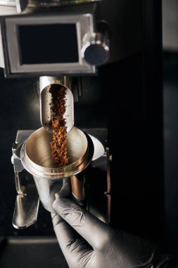 partial view of barista holding metallic measuring cup near ground coffee and coffee grinder clipart