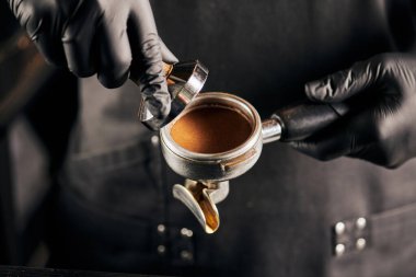 Siyah eldivenli barista 'nın elinde öğütülmüş kahve ve portafilter görüntüsü.