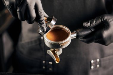 cropped view of tamper with ground coffee and portafilter in hands of barista in black gloves clipart