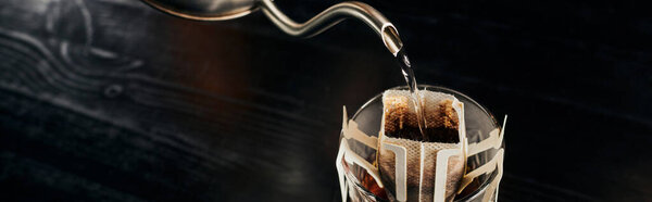 boiling water pouring from metallic kettle into glass with ground coffee in paper filter bag, banner