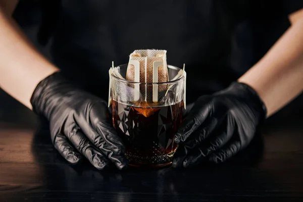 stock image barista in black latex gloves brewing espresso, glass with ground coffee in filter bag, drip method