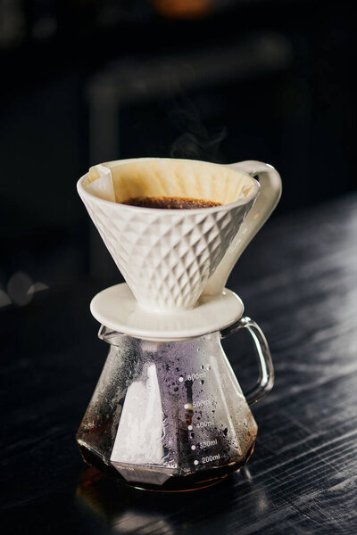 ceramic dripper with pour-over coffee on glass pot in cafe on black table, alternative V-60 style 