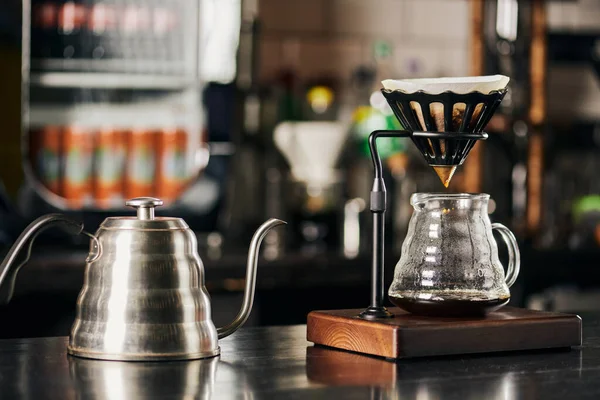 V-60 tarzı espresso birası, su damlası, kağıt filtresi olan damlatıcı tutacağı, siyah tezgahta kahve demliği.