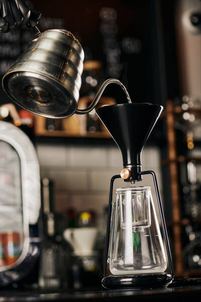partial view of barista pouring boiling water into assembled siphon coffee maker in coffee shop