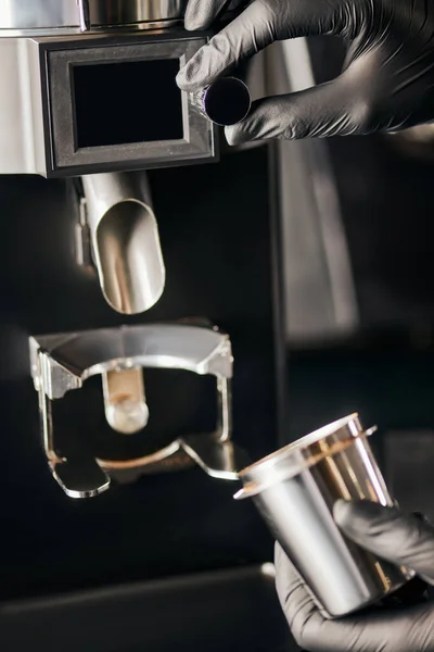 stock image cropped view of barista in black gloves with measuring cup near electric coffee grinder, equipment