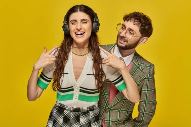 cheerful woman pointing at wireless headphones, listening music near bearded man, college students clipart