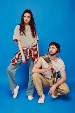 Moda bir çift, günlük kıyafetler içinde üniversite öğrencileri, kulaklıklar, müzik, kalın makyaj, mavi fon