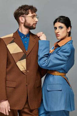 Şık bir çift, resmi giyinmiş modeller, kameraya bakıyorlar, gri arka plan, şık takımlar.