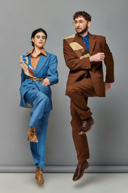 Moda pozu, gri arka planda mavi ve kahverengi takımlı mankenler, kadın ve erkek, moda çekimi.