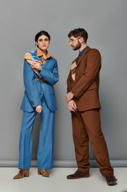 Moda pozu, gri arka planda özel takım elbiseli mankenler, resmi giyinmiş kadın ve erkek.