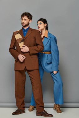 Gri arka planda poz veren takım elbiseli mankenler, resmi giyinmiş şık erkek ve kadın.
