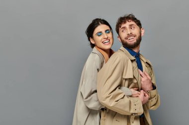 fall season, smile, romantic couple hugging on grey background, trench coats, style, bold makeup clipart