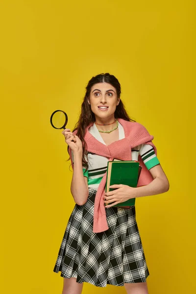 stock image curious young woman holding books and magnifier, zoom, discovery, student in college outfit, smile