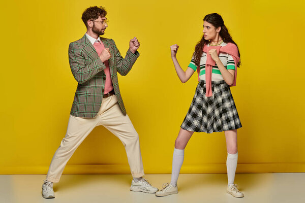 fight, man against woman, young man and woman with clenched fists, opponents, yellow backdrop