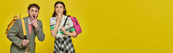 потрясенные студенты, стоящие с рюкзаками, смотрящие в камеру, прикрывающие рот, желтый фон, баннер