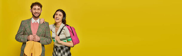 веселая женщина в беспроводных наушниках, стоящая рядом с бородатым мужчиной, студенты с рюкзаками, баннер