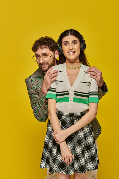 счастливая женщина в беспроводных наушниках слушать музыку рядом бородатый мужчина, смешные студенты, желтый фон