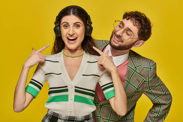 счастливая женщина указывая на беспроводные наушники, слушая музыку рядом бородатый мужчина, студенты колледжа