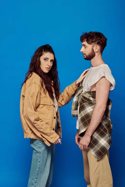 stock image fashionable couple, casual attire, blue backdrop, woman touching chest of bearded man, bold makeup