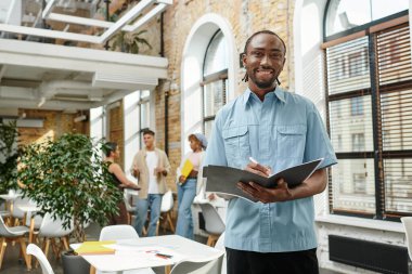 Mutlu Afro-Amerikalı adam notlar alıyor, ofis çalışanı, klasör tutuyor, fikirler yazıyor, işe koyuluyor.