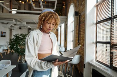 Afro-Amerikan kadın elinde klasör, belgelere bakıyor, açık alan, başlangıç projesi, gen z