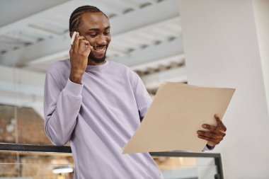 Mutlu Afro-Amerikan adam projeye kağıt üzerinde bakıyor, akıllı telefondan konuşuyor, plan yapıyor, girişimde bulunuyor.